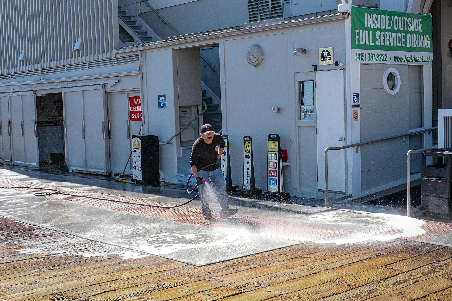 A professional pressure washing technician in safety gear cleaning the exterior wall of a modern commercial office building